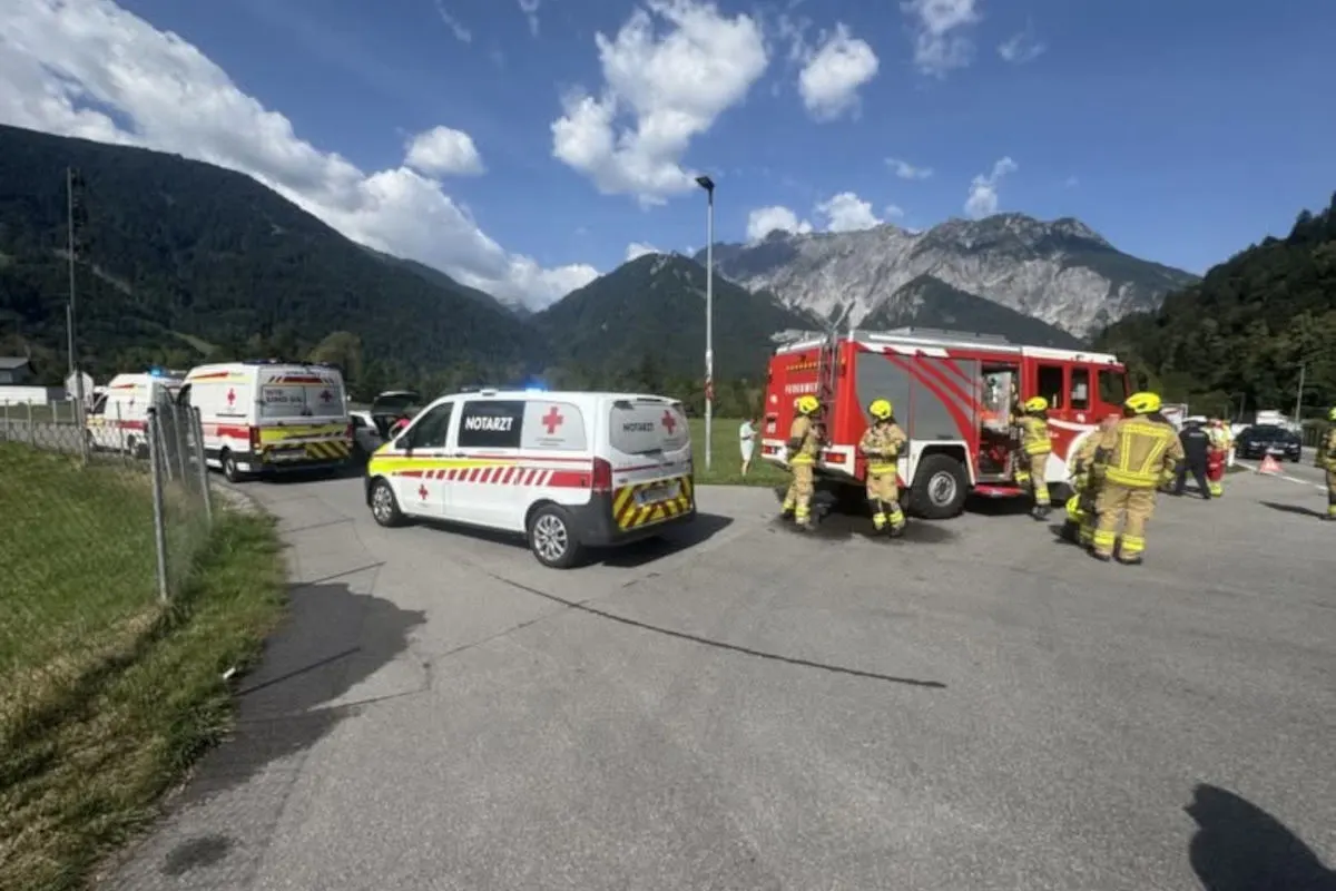 Mehrere Einsatzkräfte stehen neben Rettungsfahrzeugen und einem Feuerwehrwagen auf einer Straße in einem alpinen Gebiet bei klarem Wetter.