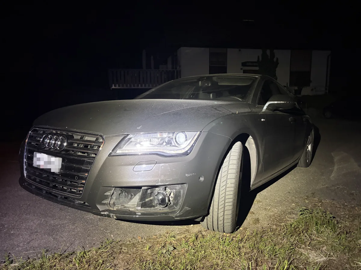 Ein grauer Audi steht bei Nacht auf einer Straße. Der Wagen hat an der Front sichtbare Schäden, insbesondere an der Stoßstange.