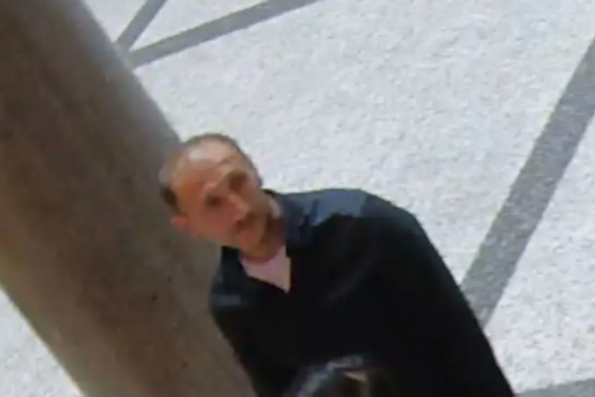 Überwachungsaufnahme zeigt eine Person, die in einem Gebäude steht. Person trägt dunkle Kleidung und schaut in Richtung der Kamera.