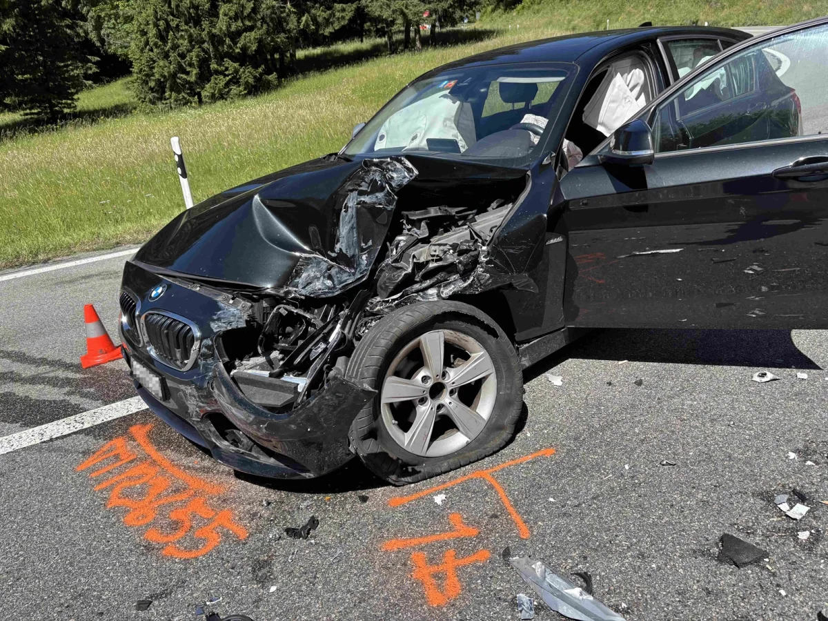 Ein schwarzer BMW mit erheblichen Frontschäden steht auf einer Landstraße. Im Hintergrund sind Verkehrsleitkegel und Gras zu sehen.