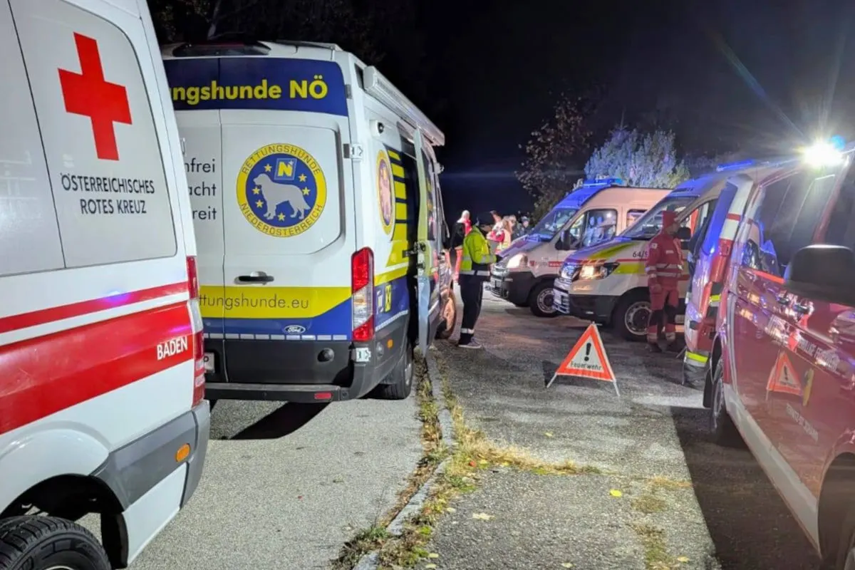 Mehrere Rettungsfahrzeuge, darunter ein Wagen des Niederösterreichischen Rettungshunde-Vereins, bei einem Nachteinsatz auf einem Parkplatz.