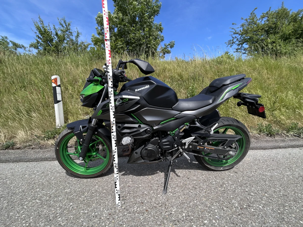 Das Bild zeigt ein schwarzes Kawasaki-Motorrad mit grünen Felgen. Es steht auf einer Landstraße neben einem Messlattenstab.