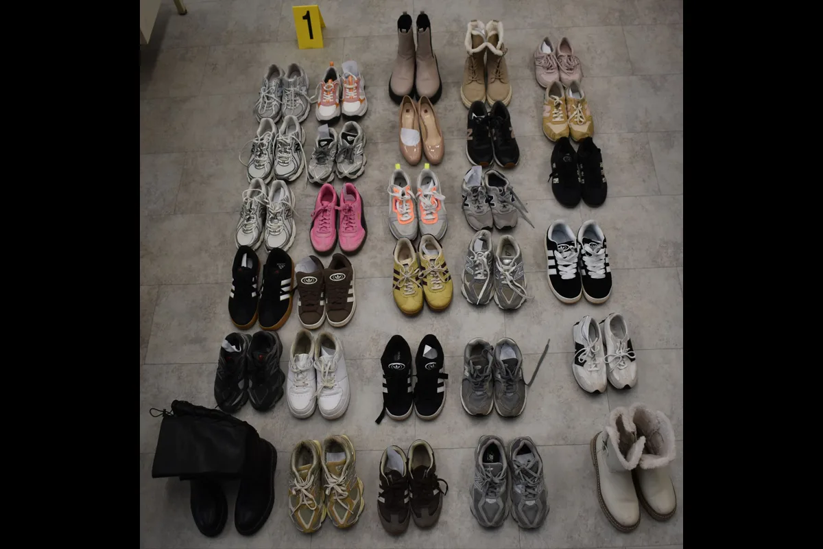 Mehrere Paar Schuhe sind in einem Raster auf dem Boden angeordnet und eine gelbe Ermittlungsmarke mit der Zahl 1 ist sichtbar.
