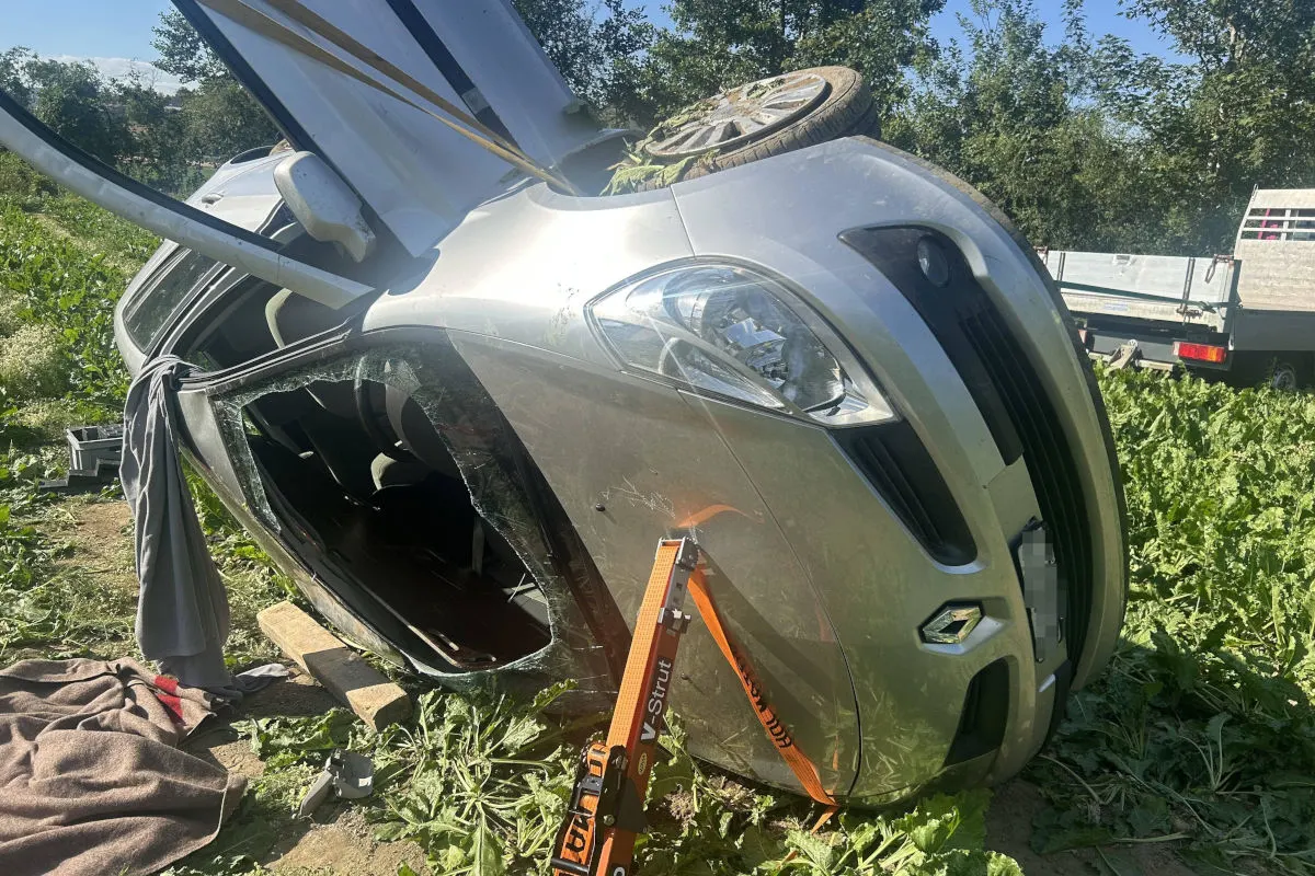 Ein silbernes Auto liegt seitlich in einem Feld, der Fensterglas ist zerbrochen, und ein Stützsystem sichert es.