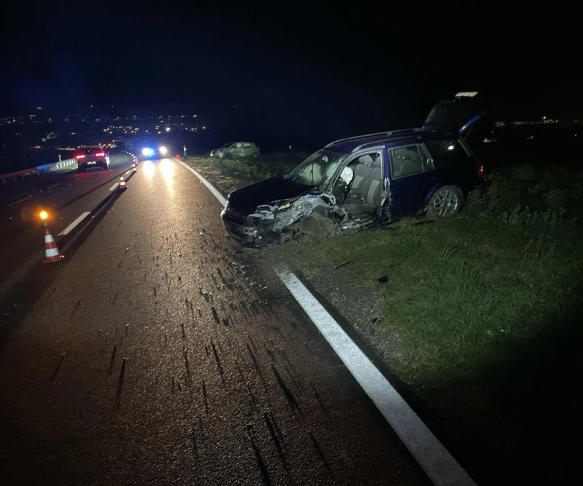 Ein stark beschädigtes Auto steht bei Nacht abseits der Straße. Im Hintergrund sind zwei weitere Fahrzeuge zu sehen.