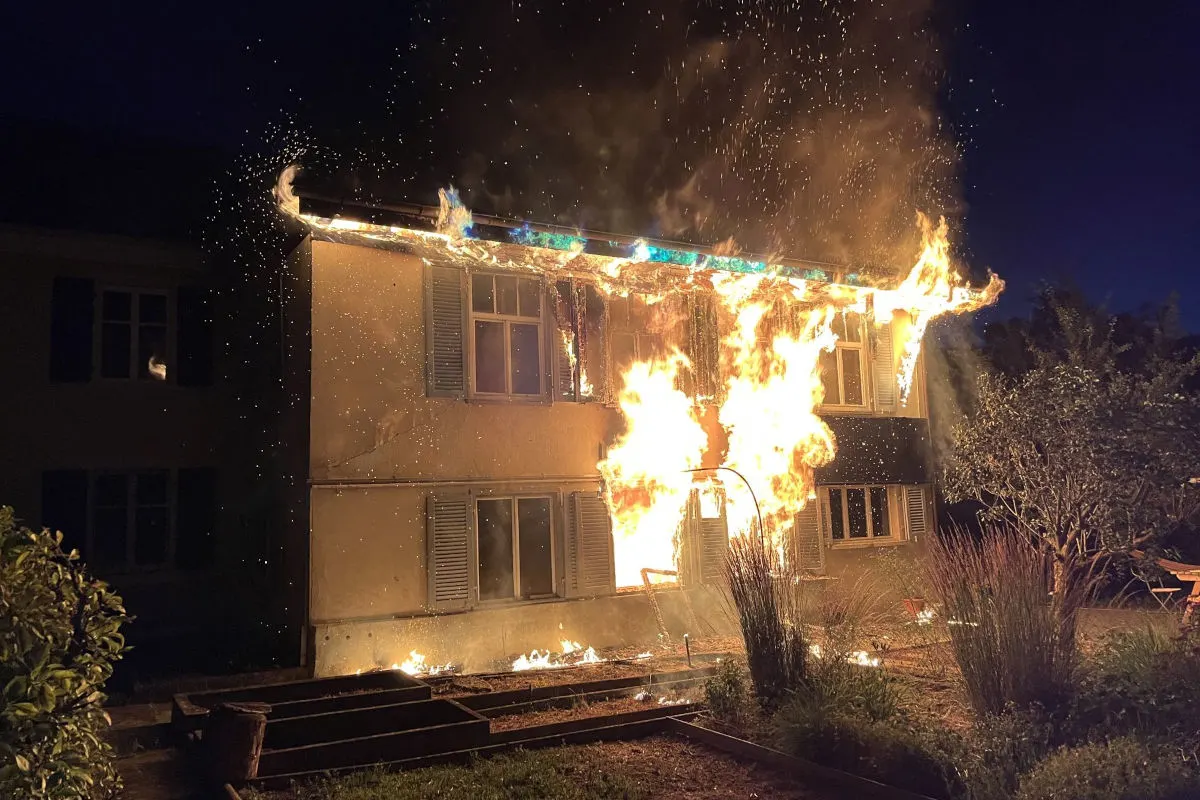 Ein Wohnhaus ist während der Nacht in Brand geraten. Flammen lodern aus dem Fenster und vom Dach.