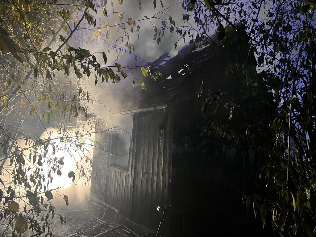 Ein Schuppen steht im Wald in Flammen, mit starker Rauchentwicklung und sichtbaren Flammen durch das Dach.