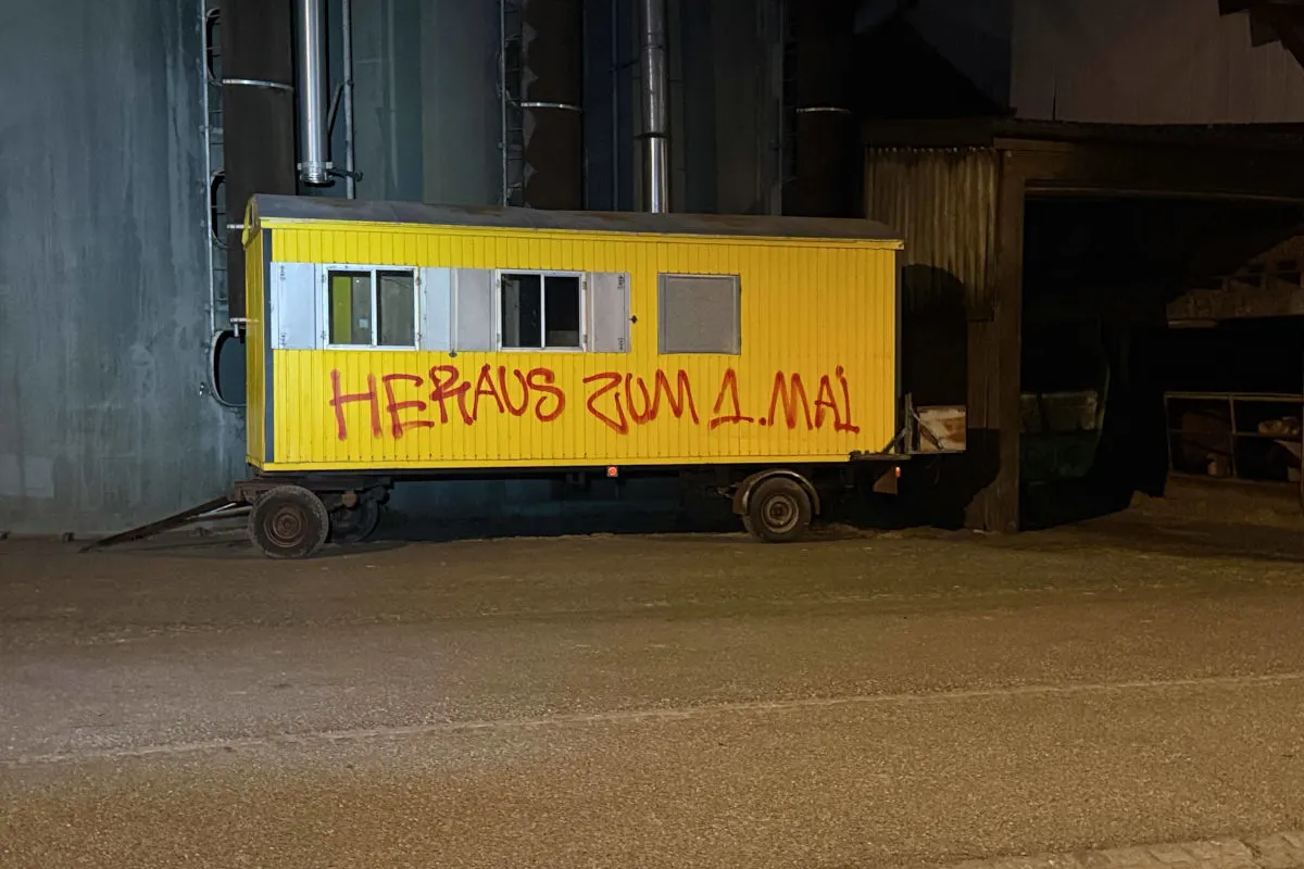 Ein gelber Bauwagen steht nachts vor einer Industrieanlage. Auf dem Wagen steht rotes Graffiti.