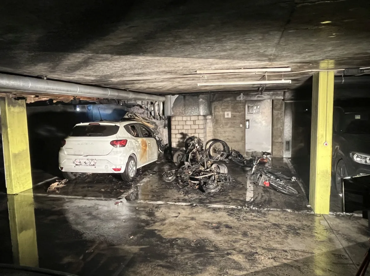 Ein weißer Pkw mit Brandschäden steht in einer Garage neben verkohlten Motorrädern auf dem Boden. Das umgebende Mauerwerk ist ebenfalls beschädigt.