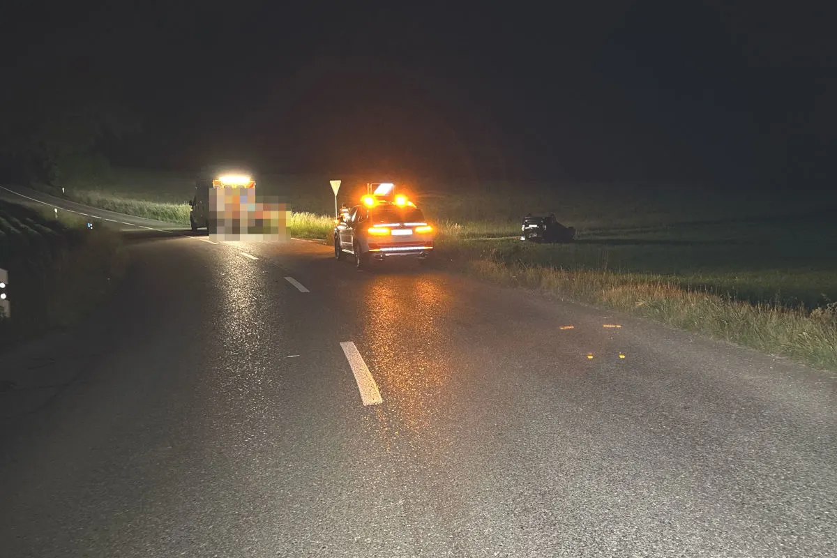 Auf einer dunklen Landstraße steht ein Auto mit eingeschaltetem Blaulicht. Im Hintergrund ist ein überschlagenes Fahrzeug erkennbar.