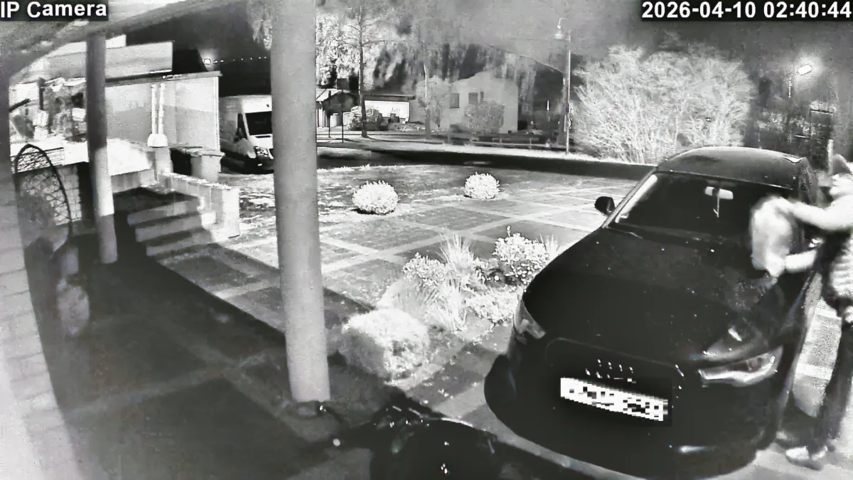 Bei Nacht ist eine Person zu sehen, die am vorderen Fenster eines geparkten Autos hantiert. Die Szene wird von einer Überwachungskamera aufgenommen.