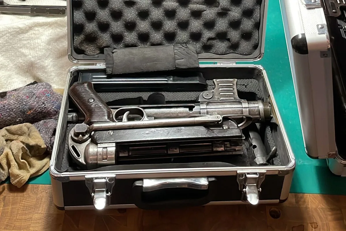 Ein offener metallener Koffer liegt auf einem Tisch und zeigt eine Schusswaffe, umgeben von Tüchern.
