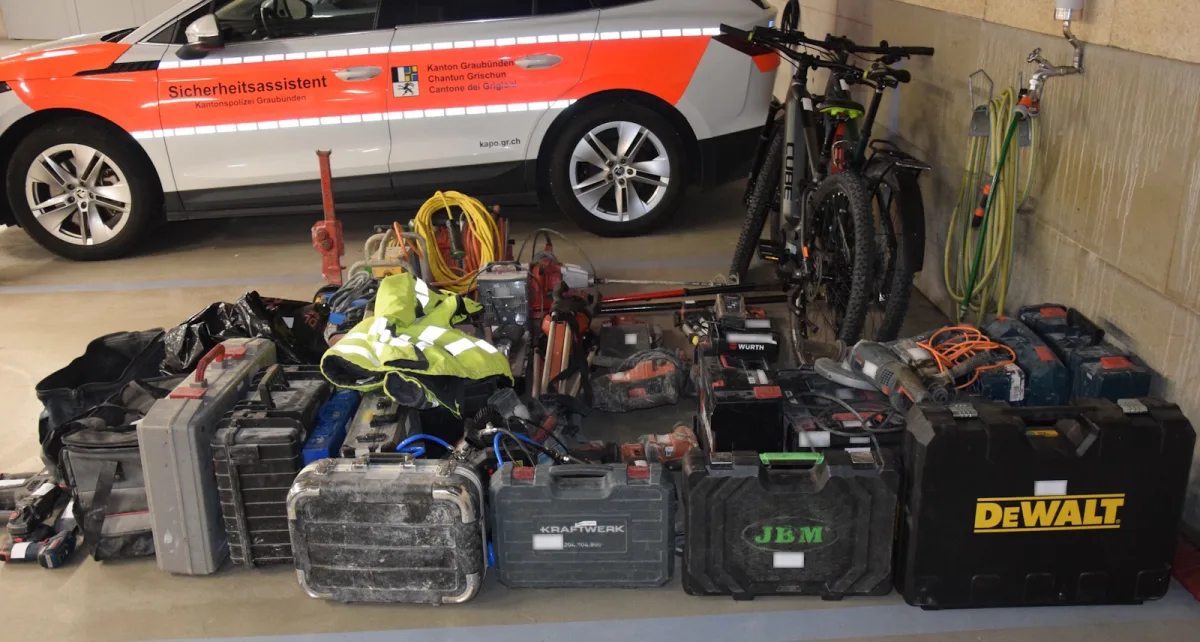 In einer Garage stehen ein Polizeifahrzeug der Kantonspolizei Graubünden und eine Vielzahl von sichergestellten Werkzeugen und Fahrrädern.