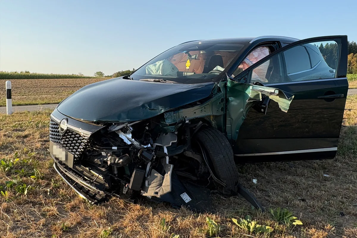 Ein Auto mit offen stehender Tür zeigt erhebliche Frontschäden nach einem Unfall auf einem Feldweg. Der Unfall ereignete sich in ländlicher Umgebung bei klarem Wetter.