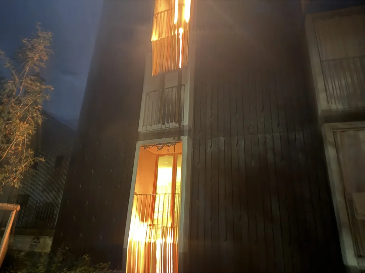 Ein Balkongeländer zeigt Flammen, die aus einer Wohnung in einem mehrstöckigen Gebäude schlagen. Es ist Nacht.