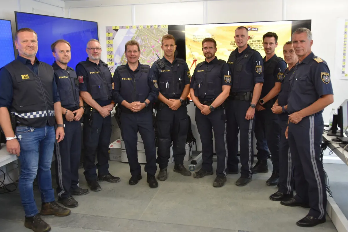 Eine Gruppe von neun Polizisten steht nebeneinander in einem Raum mit großen Monitoren im Hintergrund.
