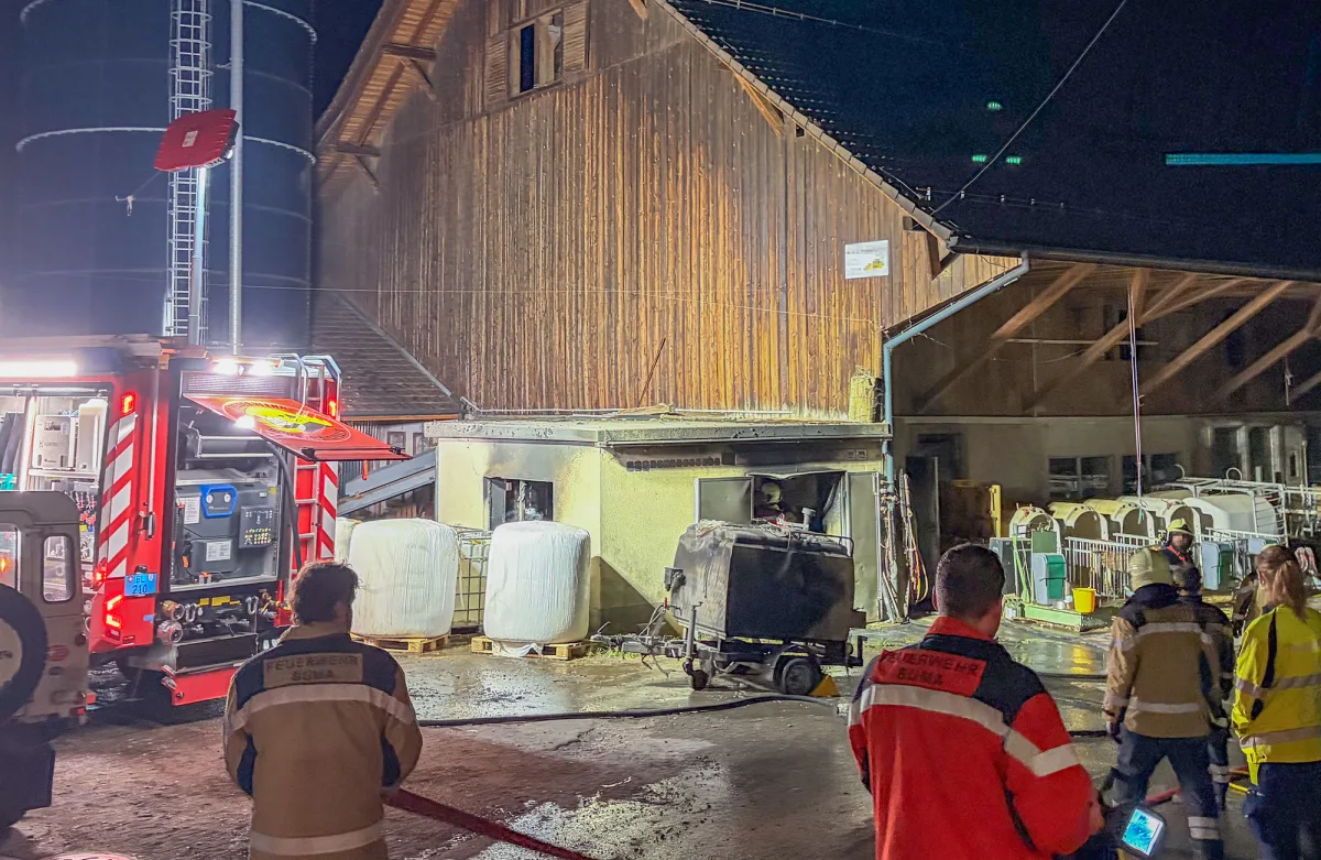 Ein Feuerwehrfahrzeug steht vor einem ländlichen Gebäude. Einsatzkräfte sind mit Löscharbeiten beschäftigt.