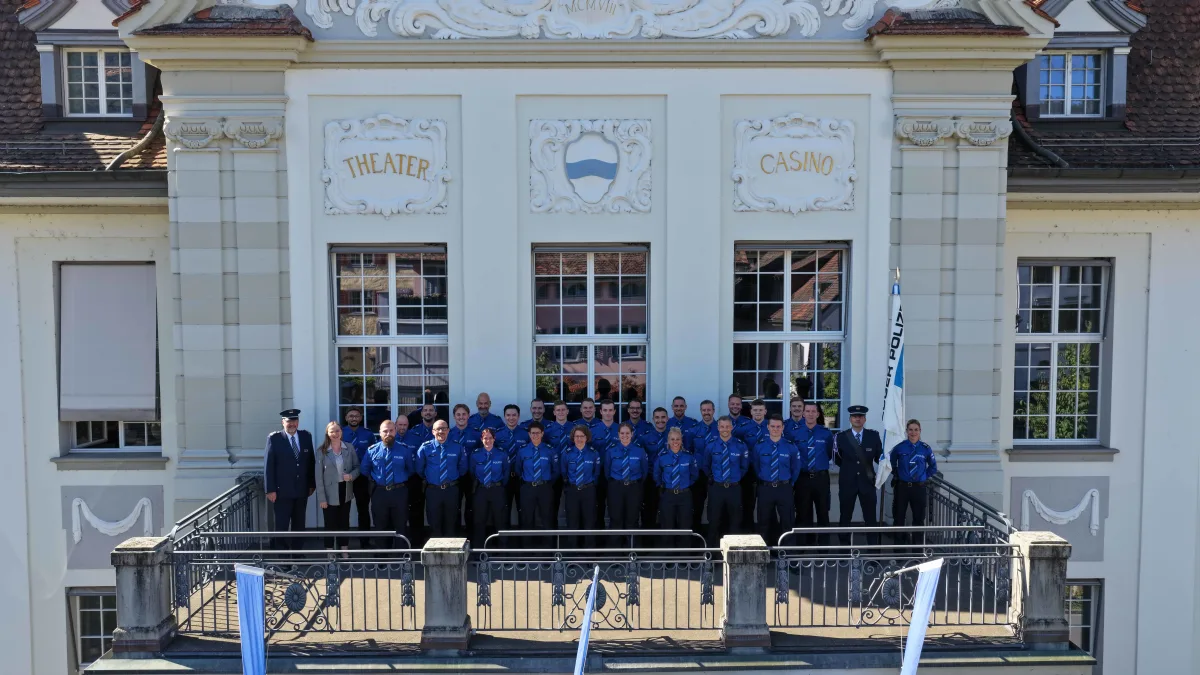 Eine Gruppe von Polizisten in blauen Uniformen steht auf einem verzierten Balkon eines historischen Gebäudes. Die Fassade zeigt das Wort 'Theater'.