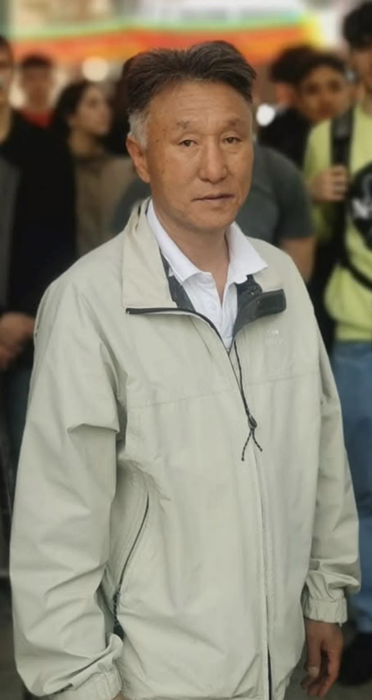 Eine Person in einer hellgrauen Jacke steht im Vordergrund, während im Hintergrund eine Menge von Menschen sichtbar ist.