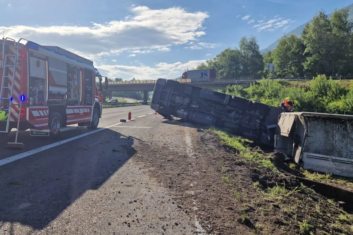 Ein umgekippter Lastwagen liegt auf der Seite auf einer Autobahn. Ein Feuerwehrfahrzeug steht daneben, während Feuerwehrleute in der Nähe arbeiten.