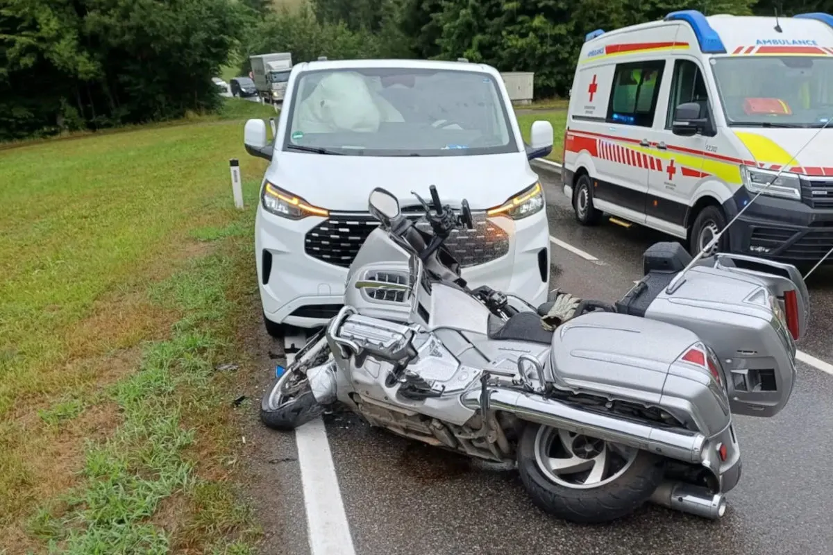 Ein silbernes Motorrad liegt umgestürzt auf der Straße vor einem weißen Van. Im Hintergrund steht ein Rettungswagen.