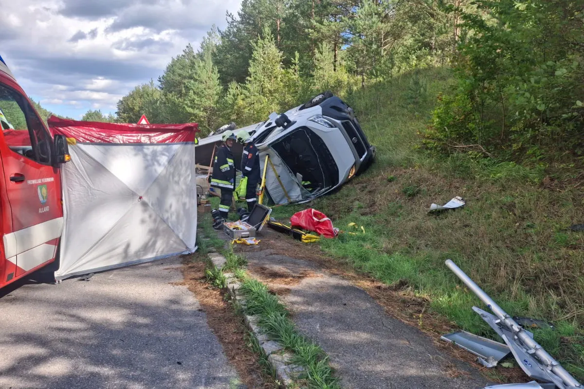 Ein umgestürzter weißer Lieferwagen liegt auf einer Böschung neben einer Straße, umgeben von Feuerwehrleuten und Ausrüstung.
