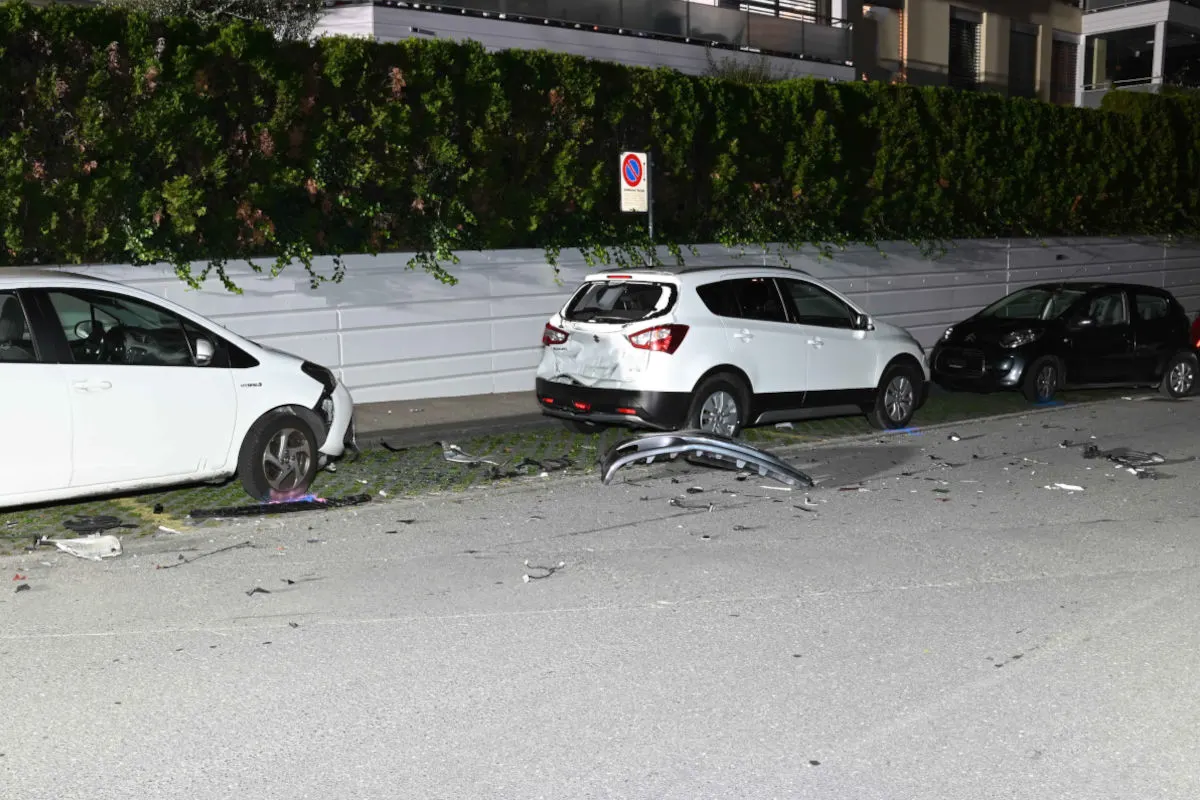 Zwei weiße Autos zeigen schwere Beschädigungen, umgeben von Trümmern, auf einer nächtlichen Straße geparkt.