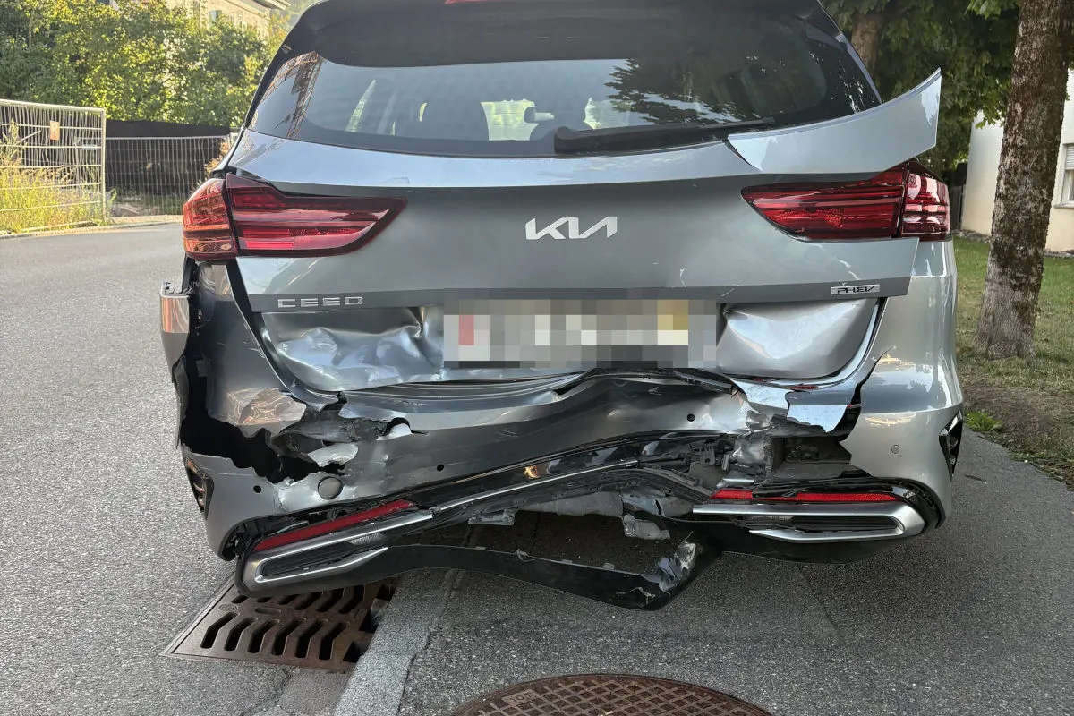 Rückansicht eines grauen Kia Ceed mit schweren Schäden am Heck. Das Fahrzeug steht am Straßenrand bei Tageslicht.