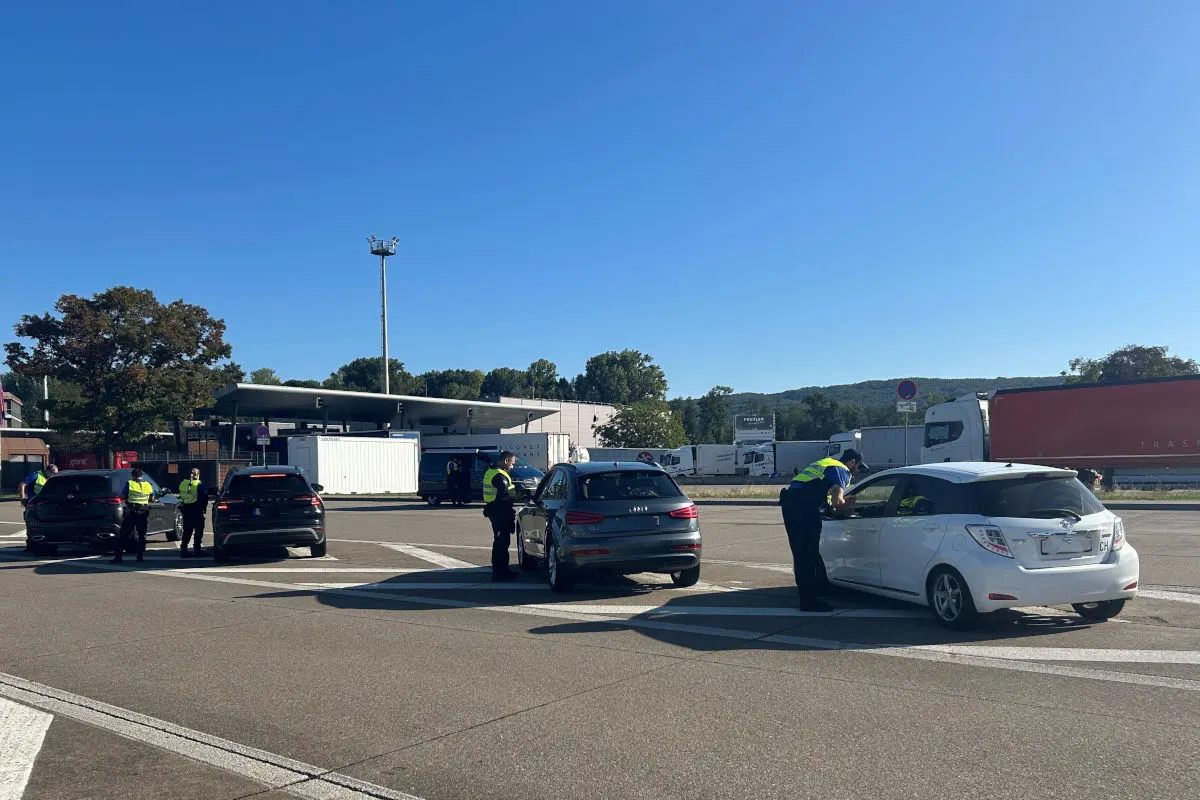 Mehrere Polizeibeamte kontrollieren Fahrzeuge an einer Raststätte bei klarem Wetter. Einige Beamte sprechen mit den Autofahrern.