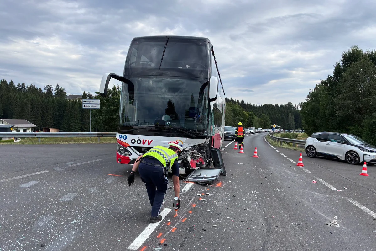 Ein beschädigter Reisebus auf einer Autobahn, umgeben von Verkehrsleitkegeln. Ein Polizist sichert die Unfallstelle ab.