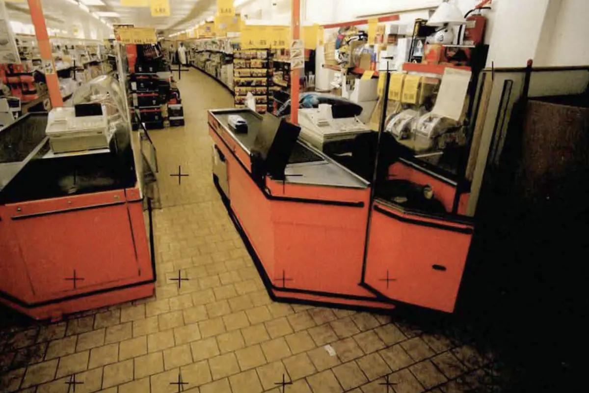 Das Bild zeigt zwei leere Kassenbereiche in einem Supermarkt. Die Gänge im Hintergrund sind ebenfalls leer und die Beleuchtung ist eingeschaltet.