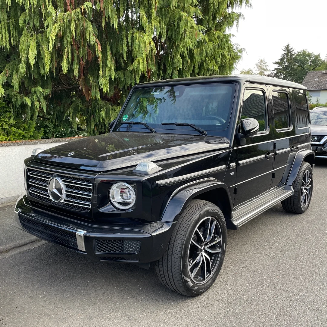 Ein schwarzer Mercedes-Geländewagen parkt am Straßenrand. Im Hintergrund sind Bäume sichtbar.
