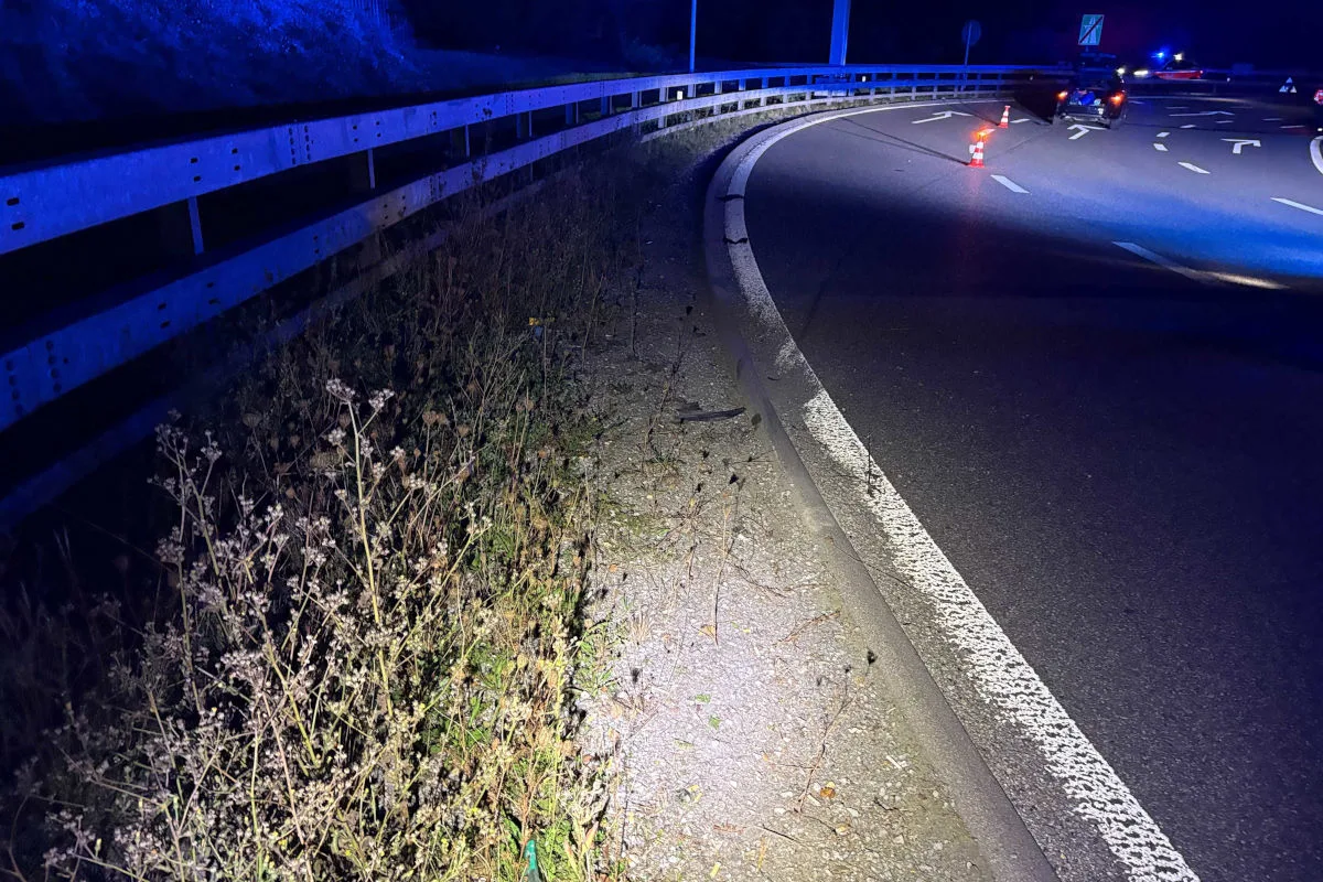 Eine kurvige Straße bei Nacht mit sichtbaren Leitplanken und Verkehrsleitkegeln, beleuchtet durch Scheinwerfer.