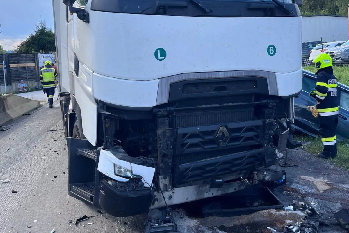 Ein weißer Lkw mit stark beschädigter Front steht auf der Straße. Feuerwehrleute arbeiten am Unfallort.