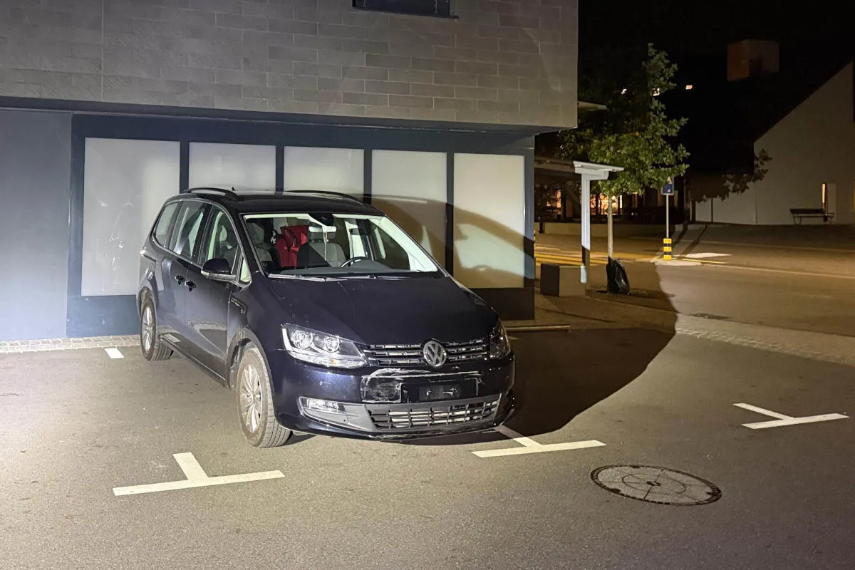 Ein blaues VW-Auto ist vor einem Gebäude in einem beleuchteten Bereich geparkt. Es ist Nacht, und das Fahrzeug ist deutlich sichtbar im Scheinwerferlicht.