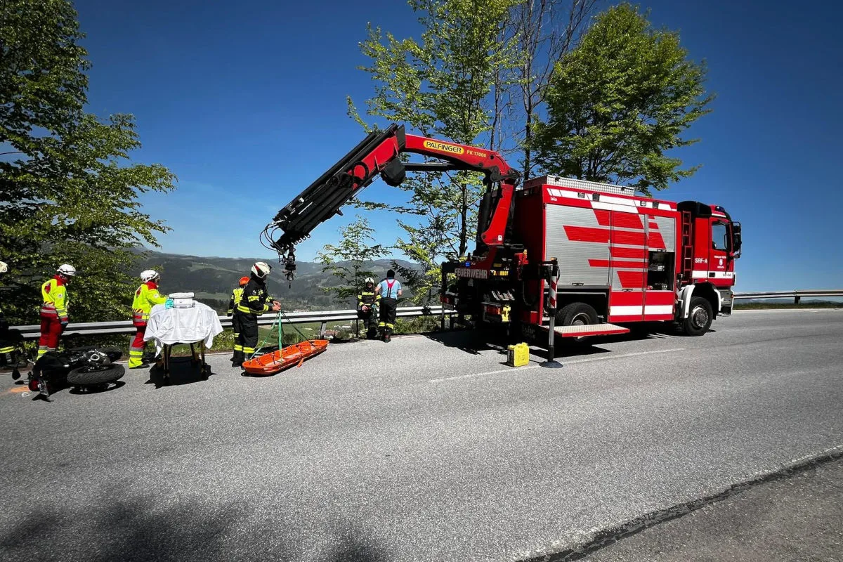 Ein rotes Feuerwehrfahrzeug mit Kran steht auf einer Straße. Einsatzkräfte bereiten einen Rettungseinsatz vor, erkennbar an Tragen und Schutzausrüstung.