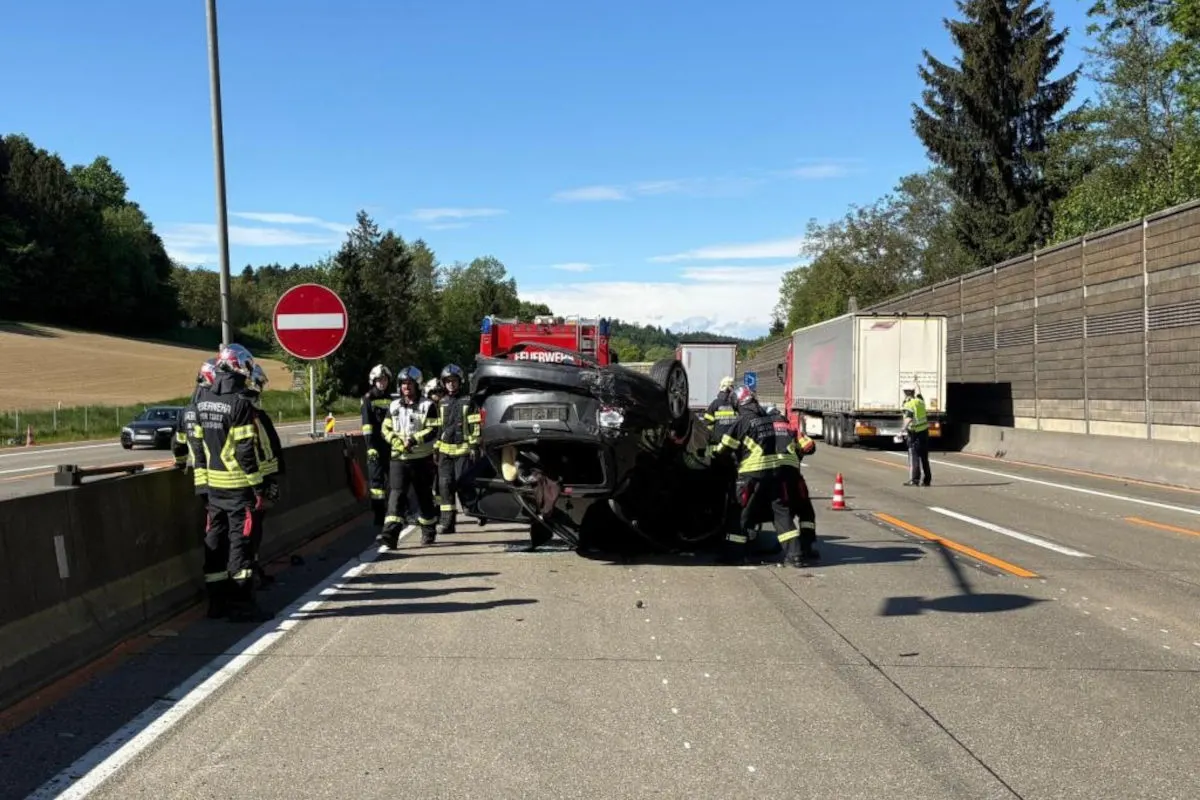Mehrere Feuerwehrleute stehen um ein umgekipptes Auto auf der Autobahn. Im Hintergrund sind ein Lkw und Verkehrsschilder zu sehen.