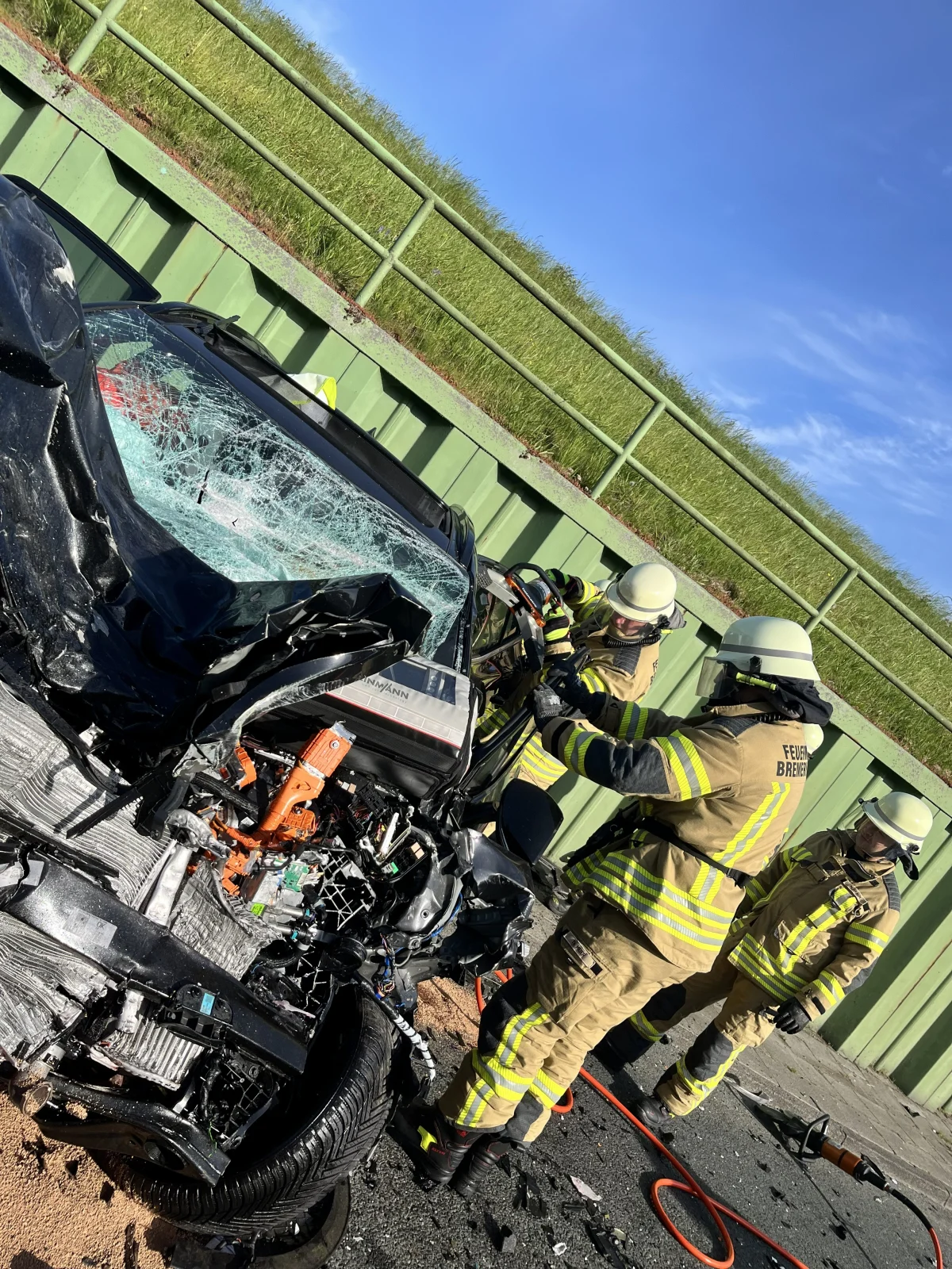 Mehrere Feuerwehrleute in Schutzkleidung arbeiten an einem stark beschädigten Auto, um Insassen zu befreien.