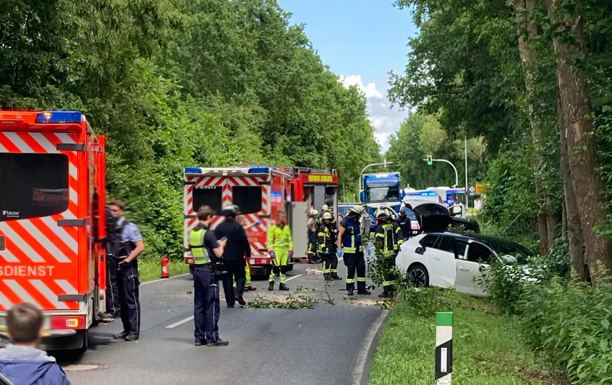 Rettungskräfte und Polizisten sind an einem Unfallort auf einer Straße in einem Waldgebiet, wo ein weißes Auto verunfallt ist.
