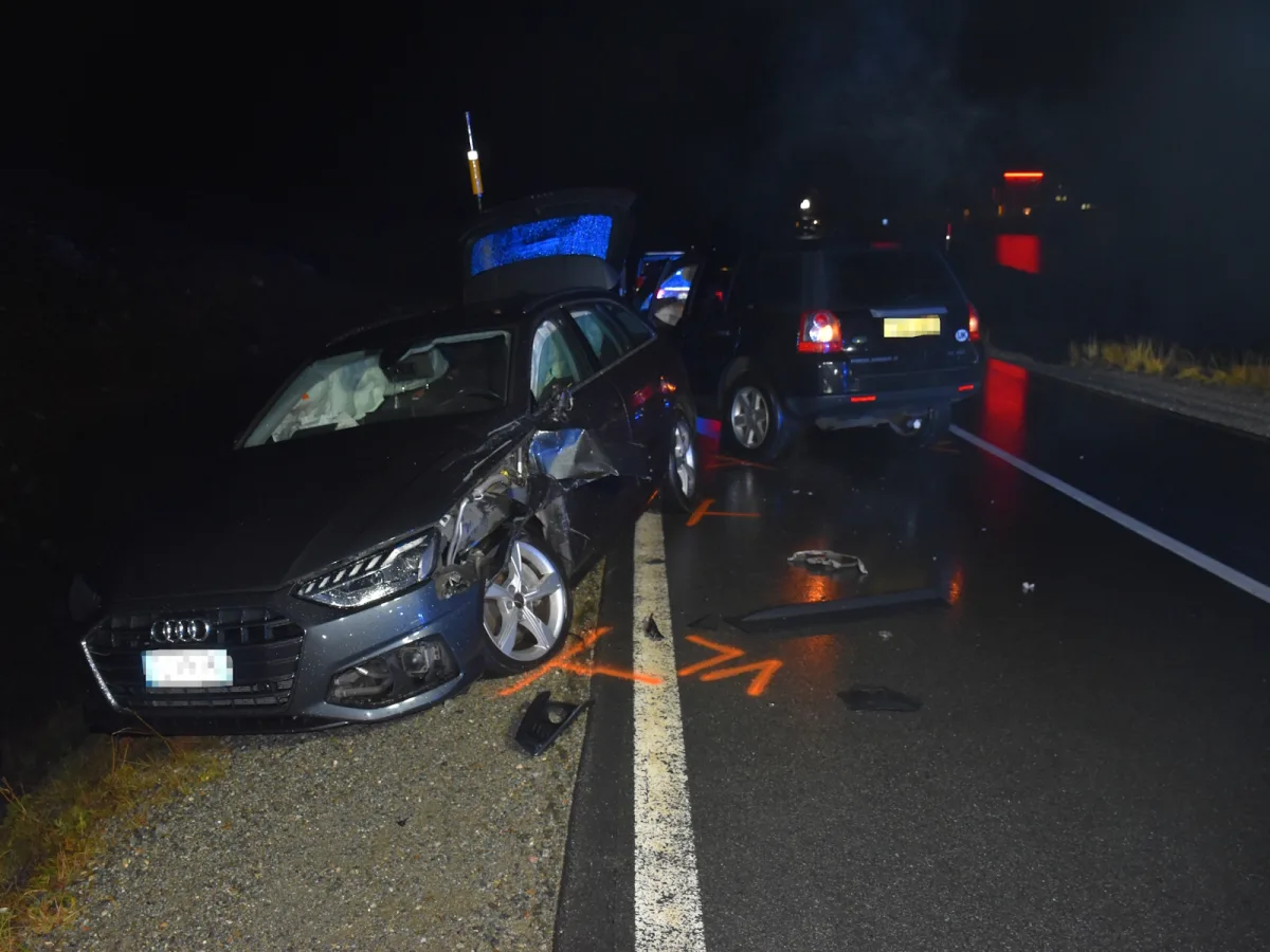 Zwei Fahrzeuge, darunter ein Audi mit Schäden an der Vorderseite, stehen auf nasser, beleuchteter Straße bei Nacht.