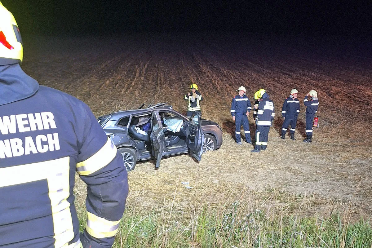 Mehrere Feuerwehrleute stehen neben einem beschädigten Auto auf einem Feld. Es ist Nacht und das Auto hat offene Türen.