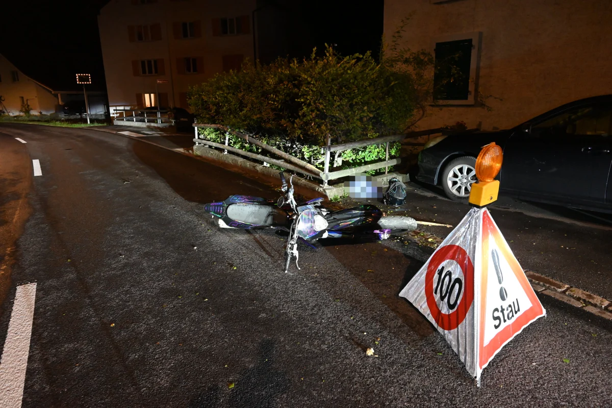 Ein Motorroller liegt umgestürzt auf einer leicht beleuchteten Straße. Daneben steht ein Verkehrszeichen, das auf Stau hinweist.