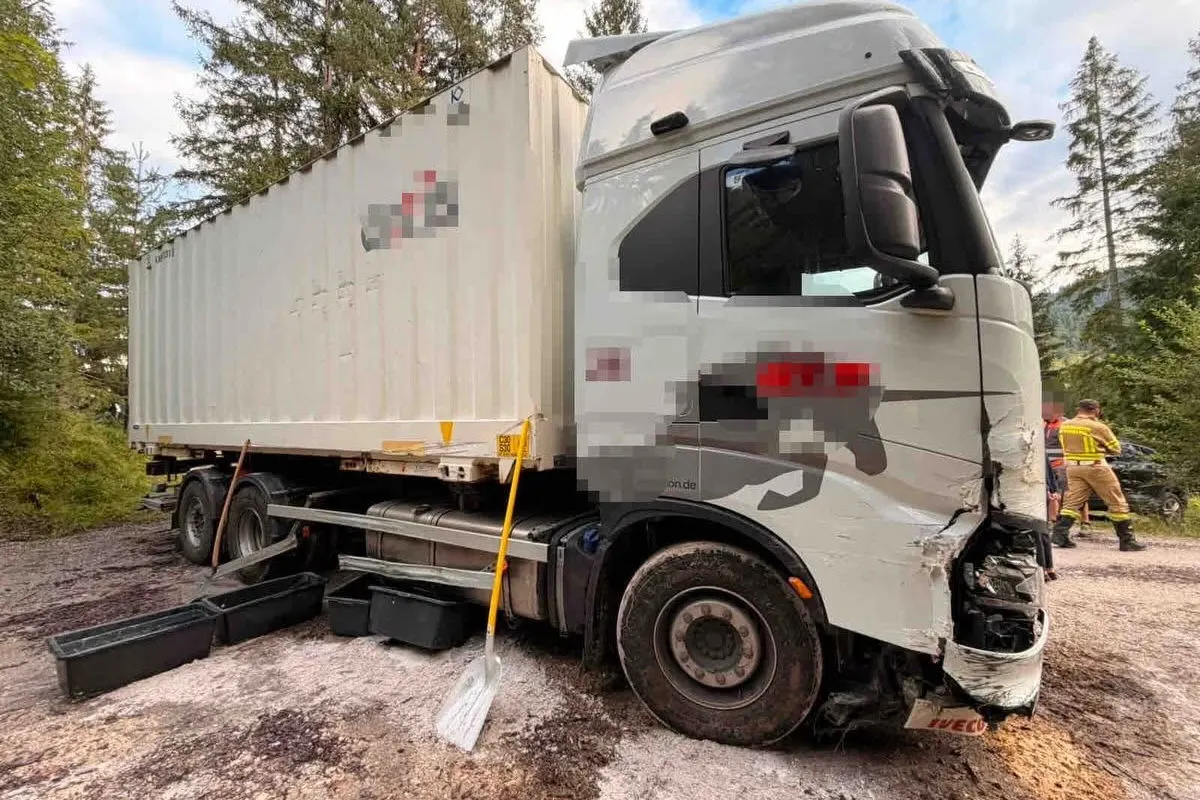 Ein LKW mit Frontschaden steht auf einem Waldweg, daneben schwarze Kisten und Schaufel, umgeben von Bäumen.