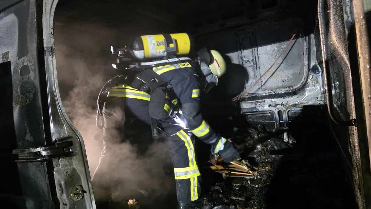 Ein Feuerwehrmann in voller Schutzausrüstung löscht einen Brand im Inneren eines Transporters, Rauch ist sichtbar.