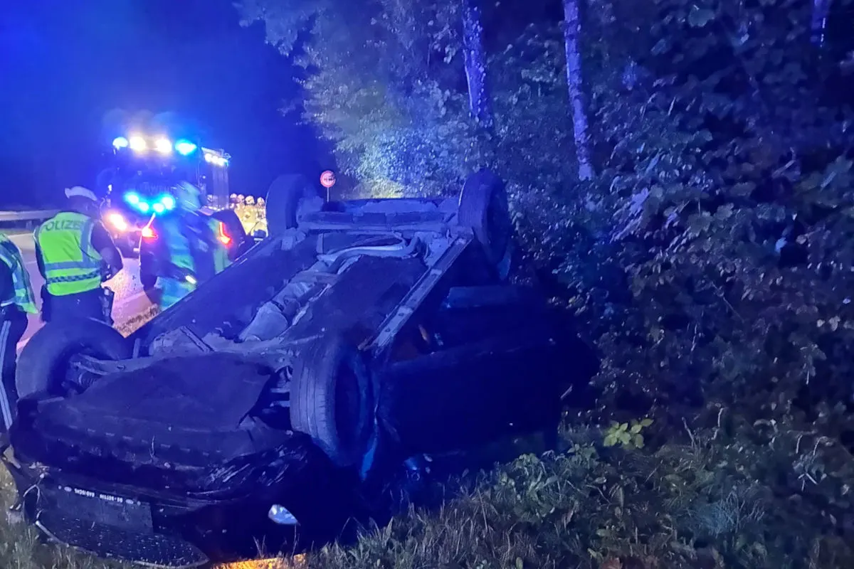 Auf einer nächtlichen Straße liegt ein Auto auf dem Dach in einem Graben. Polizeibeamte in Warnwesten stehen daneben.