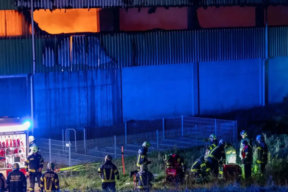 Mehrere Feuerwehrleute sind in der Nacht vor einem brennenden Gebäude im Einsatz. Flammen sind im oberen Teil des Gebäudes sichtbar.