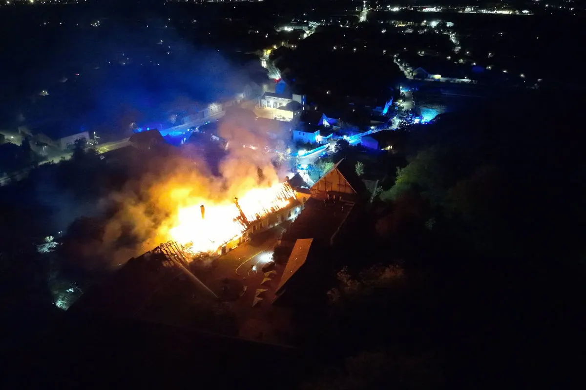 Luftaufnahme bei Nacht zeigt ein Gebäude, das in Flammen steht, umgeben von dichtem Rauch und Notfallbeleuchtung.