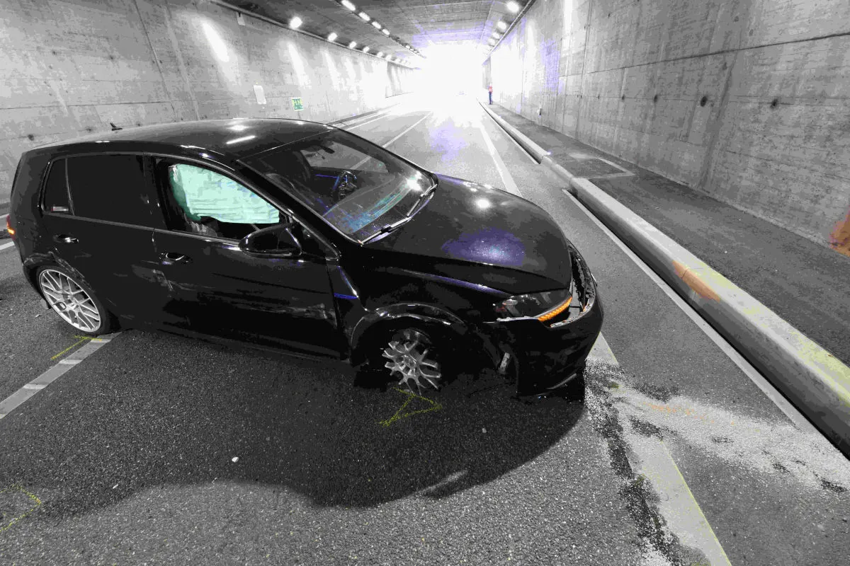 Ein schwarzes Auto zeigt deutliche Unfallspuren im Frontbereich und steht quer in einem Tunnel. Der Tunnel ist asphaltiert und gut beleuchtet.