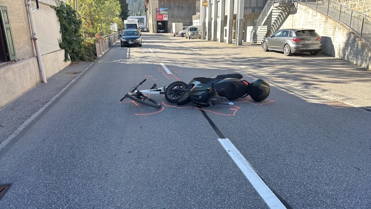 Ein E-Bike und ein Fahrrad liegen nach einem Unfall mitten auf einer urbanen Straße. Hinter ihnen sind geparkte Autos und Gebäude zu sehen.