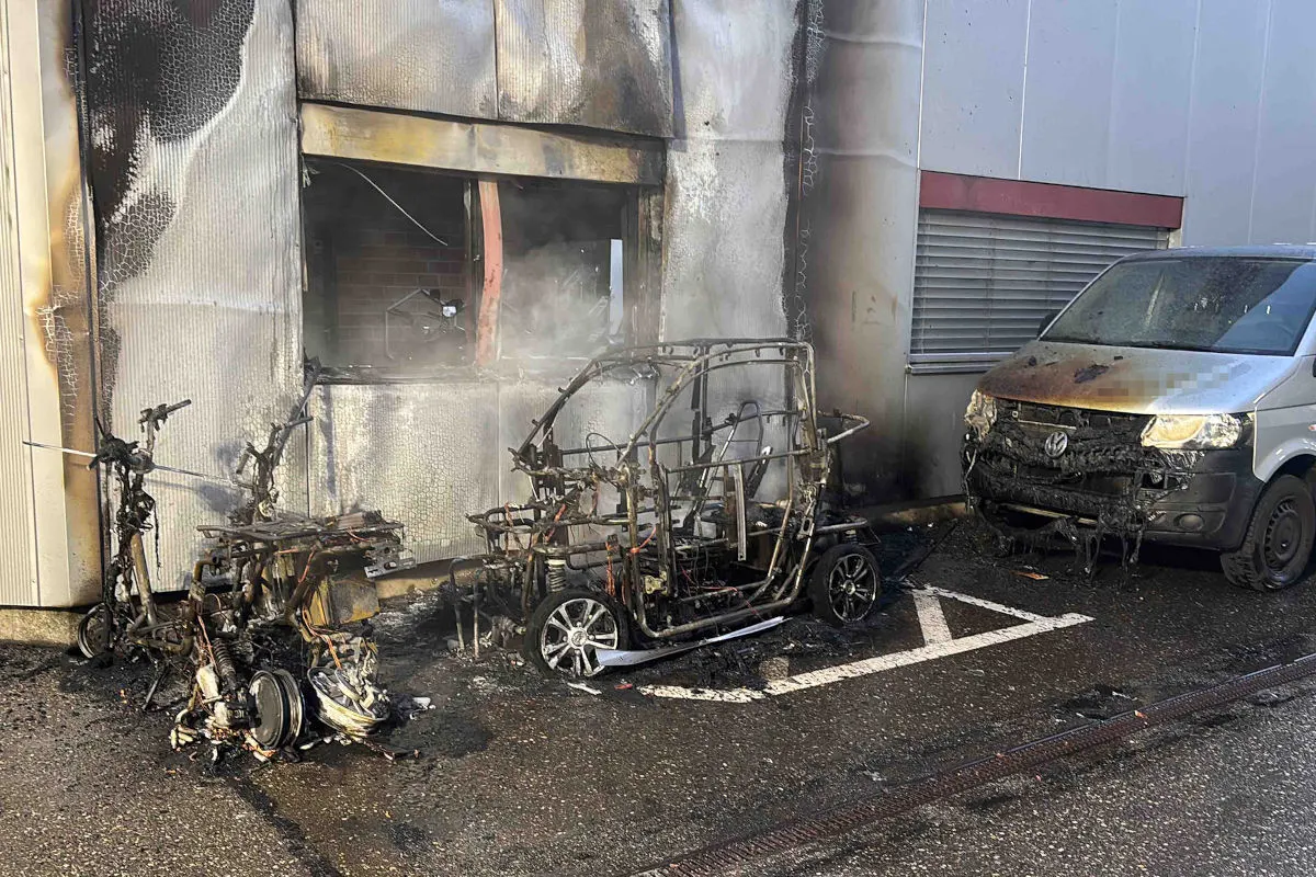 Mehrere verbrannte Fahrzeuge stehen vor einem beschädigten Gebäude. Ein Transporter zeigt Brandschäden an der Front.